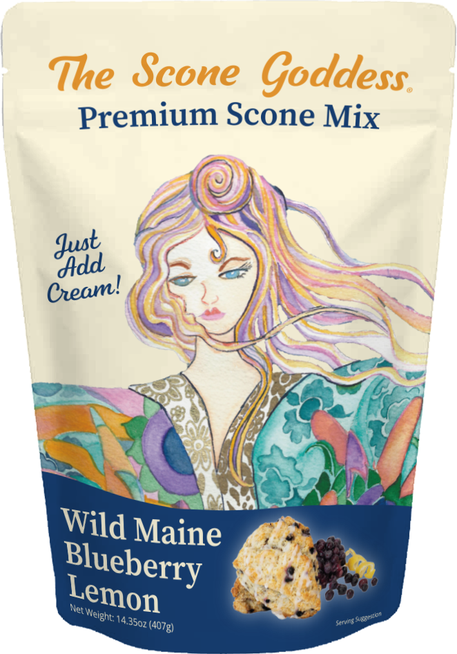 A stand-up pouch of The Scone Goddess Premium Scone Mix, Wild Maine Blueberry Lemon flavor. The packaging features a cream-colored top section with orange and blue text, and a colorful illustration of a woman with flowing hair.