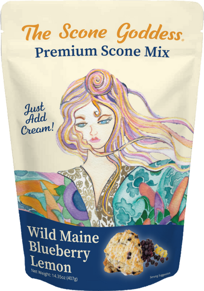 A stand-up pouch of The Scone Goddess Premium Scone Mix, Wild Maine Blueberry Lemon flavor. The packaging features a cream-colored top section with orange and blue text, and a colorful illustration of a woman with flowing hair.